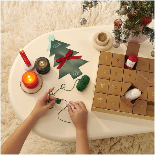 Person crafting with yarn on a table near a Christmas-themed advent calendar.