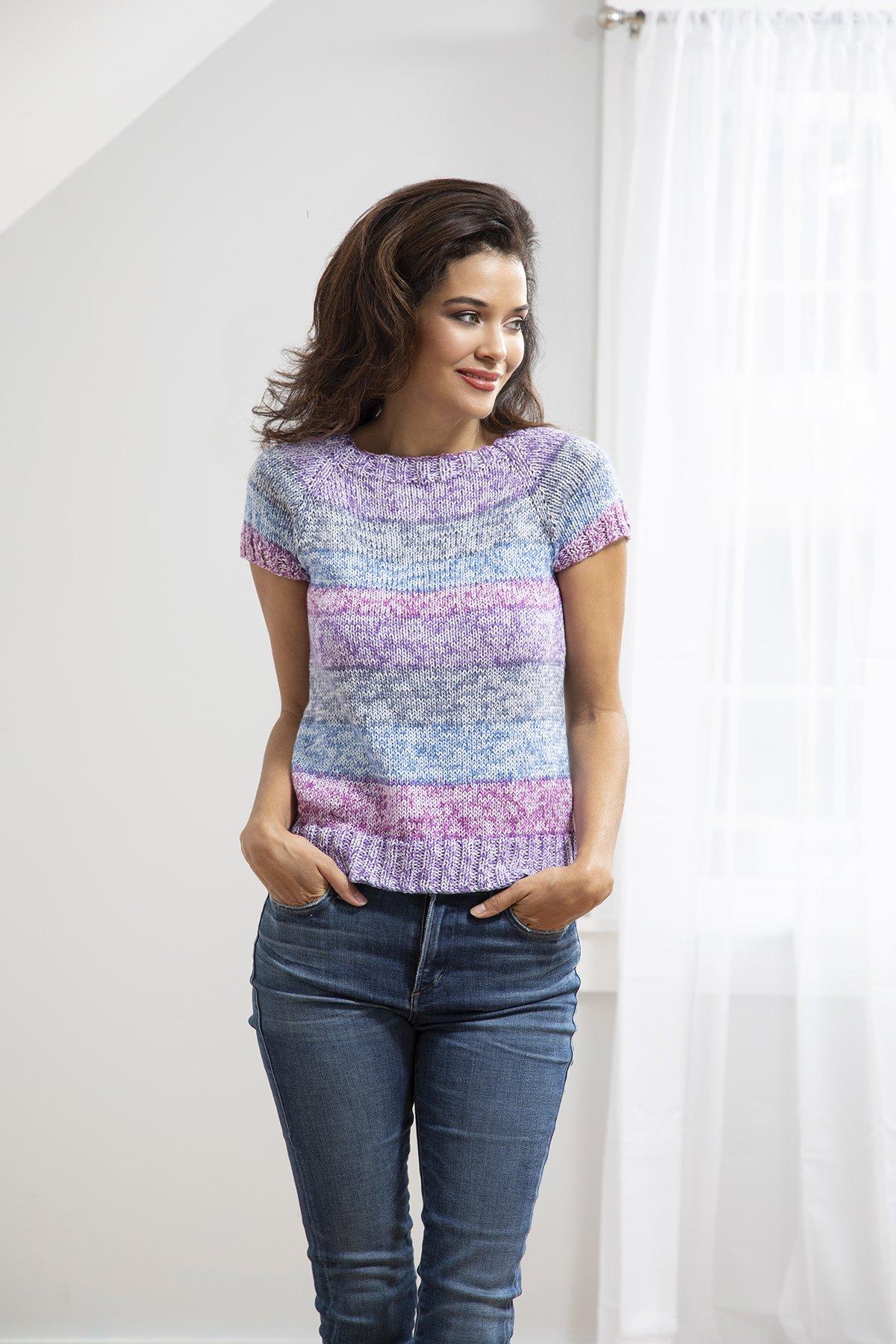 Woman wearing a colorful knitted top and blue jeans against a white background