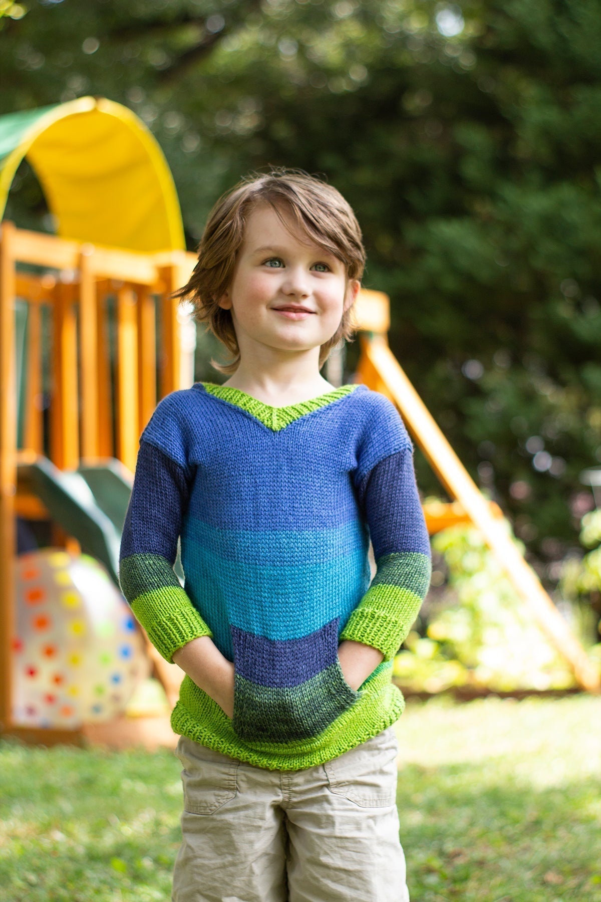 Child wearing a colorful sweater standing outdoors with playground equipment in the background