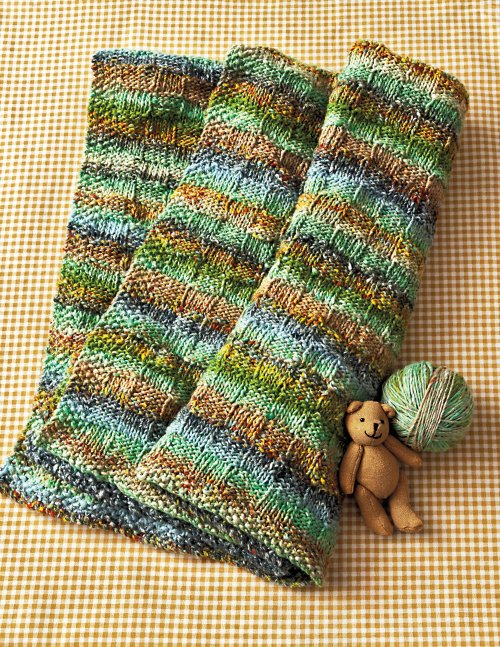 Knitted green and brown striped blanket with a small teddy bear on a checkered background