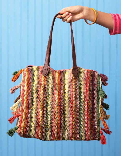 Colorful striped handbag with tassels held by a hand against a blue background