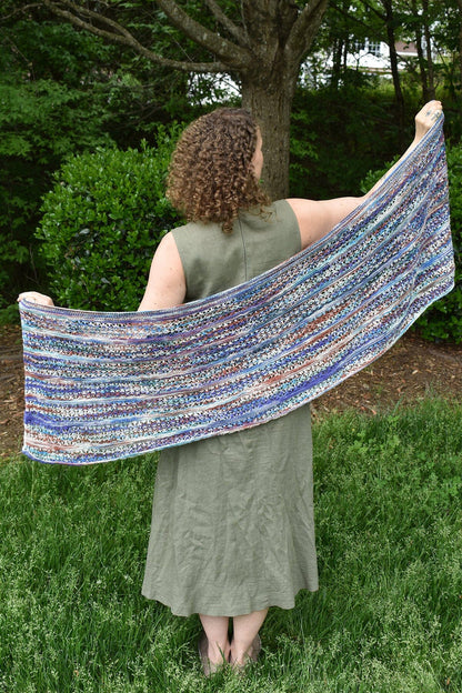 Woman holding a colorful shawl outdoors in a garden setting