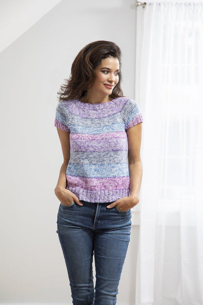 Woman wearing a colorful knitted top and blue jeans against a white background