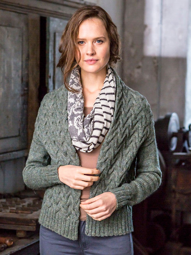 Woman wearing a green knitted cardigan with a patterned scarf in a rustic setting
